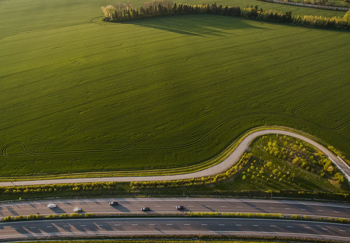 A picture of a highway next to a large green field. There are several cars on the highway