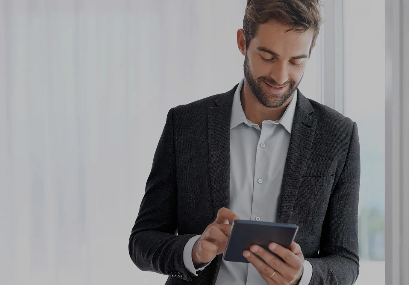 A man in business attire is looking at a tablet next to a window