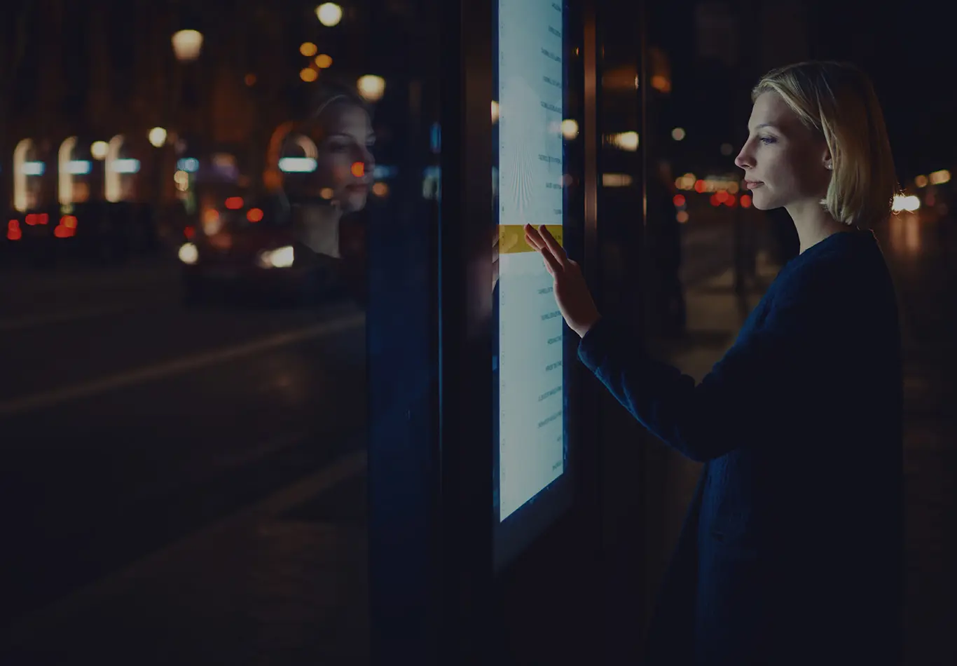 A woman is interacting with a public touch screen at night