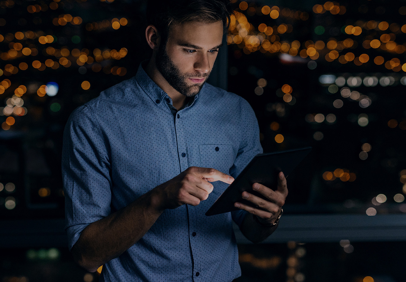 A man with facial hair is looking at a tablet at night