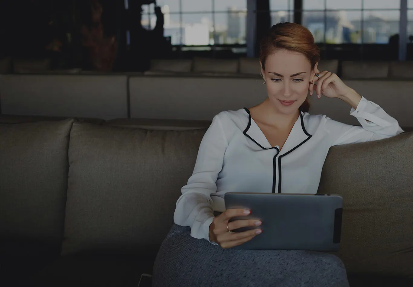 A woman is sitting on her couch reading a tablet