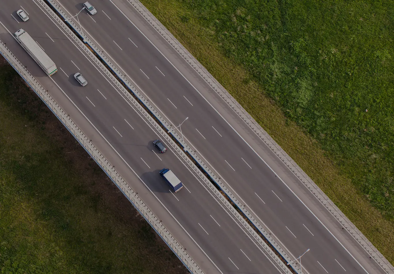 Aerial view of a highway. There are a few cars and trucks on it. 