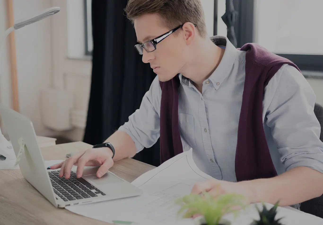 A man with short brown hair and glasses is working on a computer