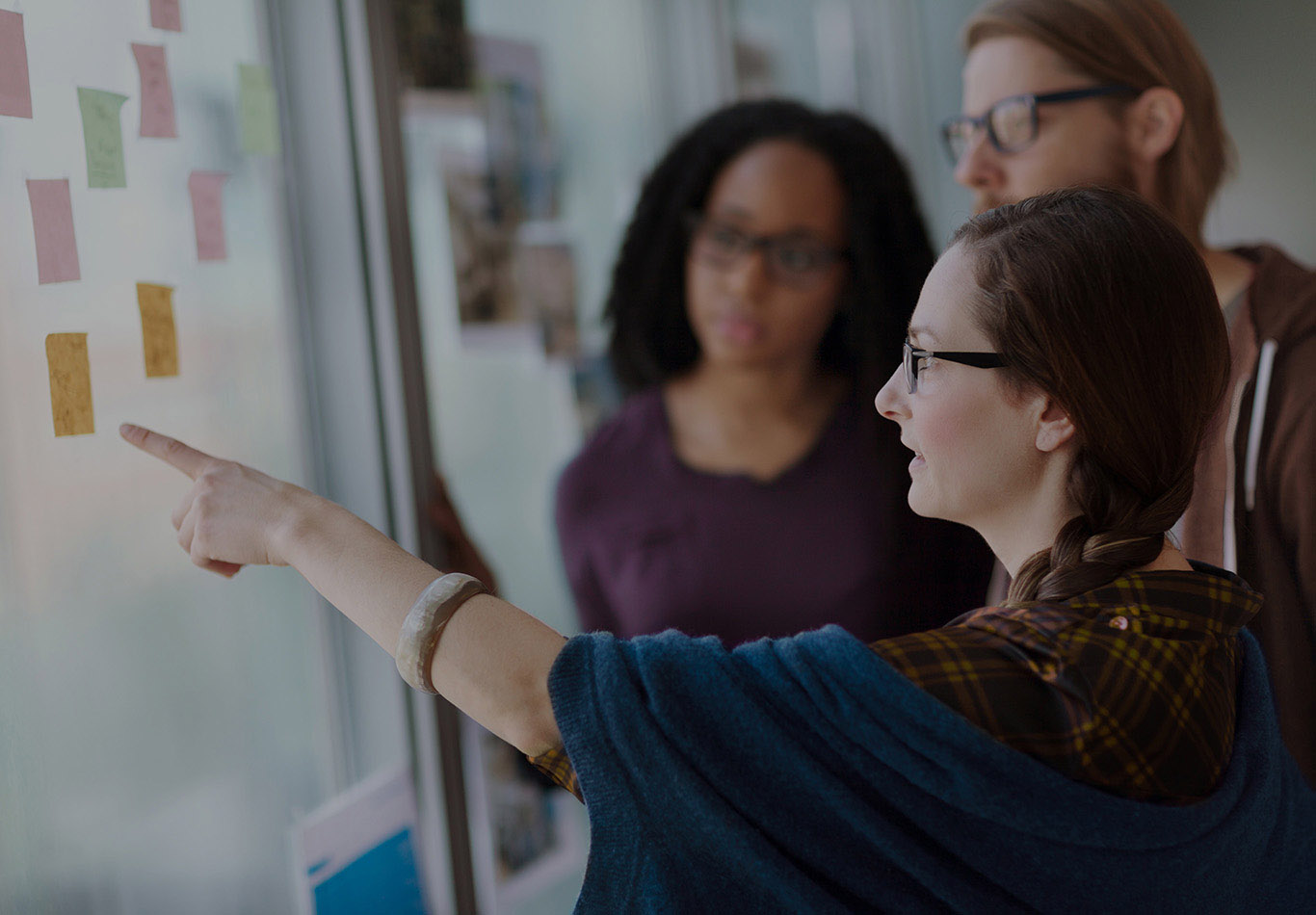 three business colleagues discussing something. One business person is pointing to a post-it notes