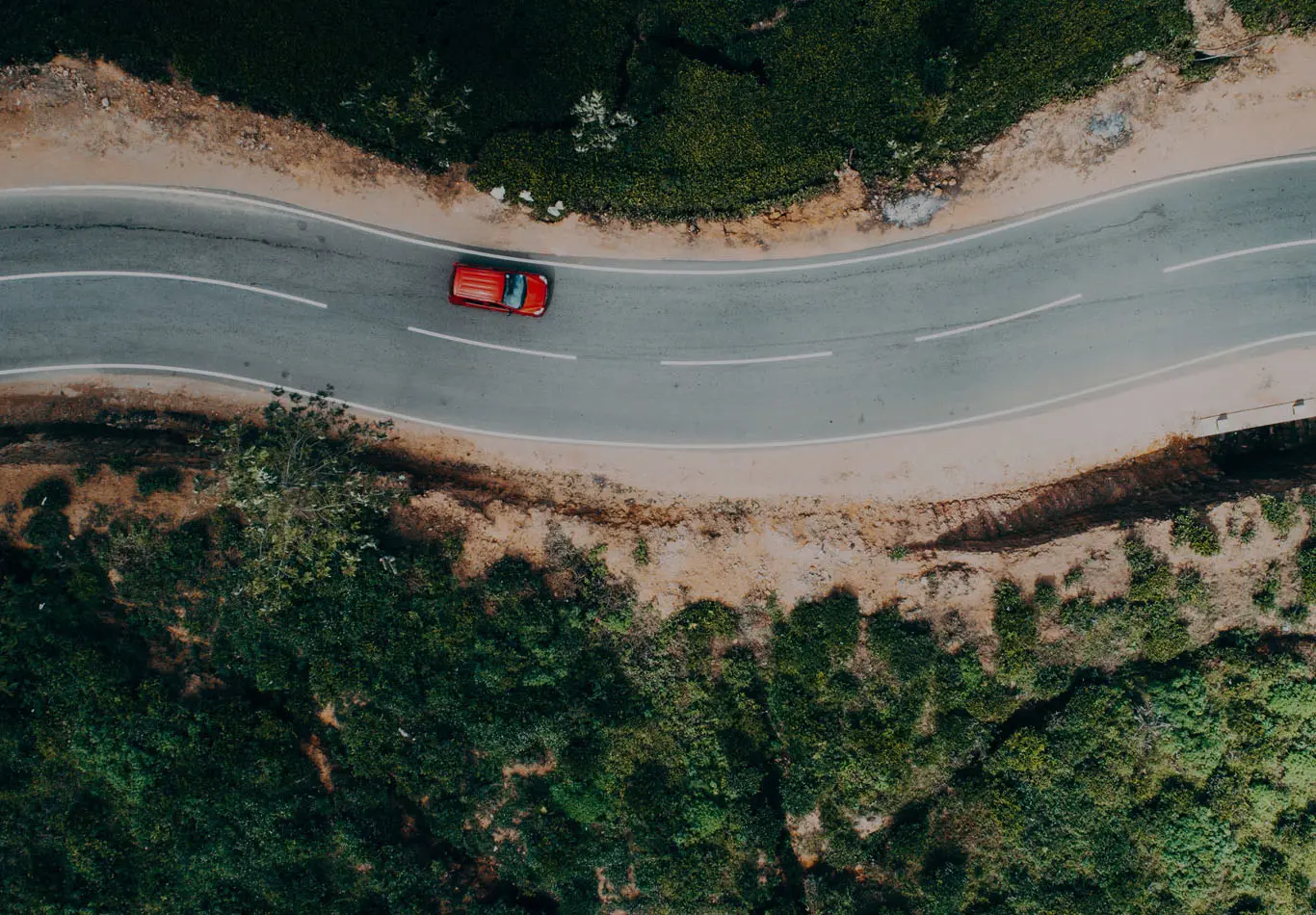 A red car is driving on a winding road. 