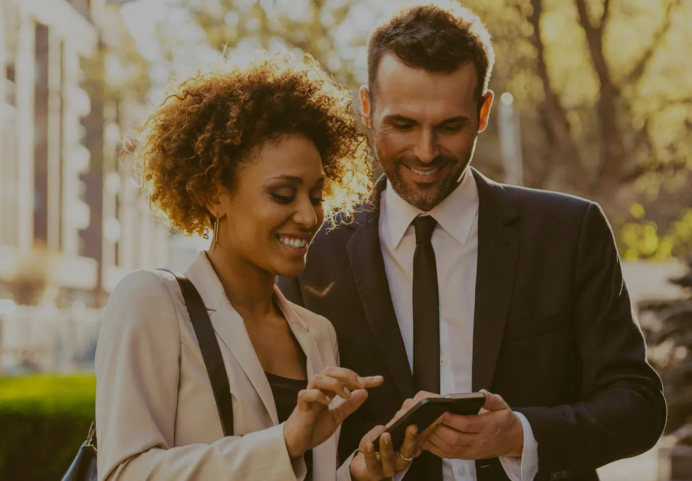 A business person and a business woman are standing next to each other and looking at their respective phones