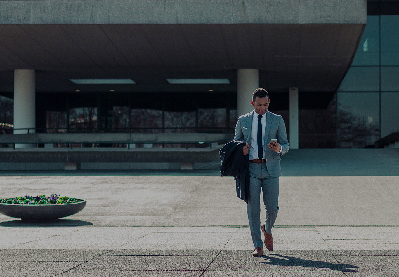 A business man is walking and looking at his phone during the day