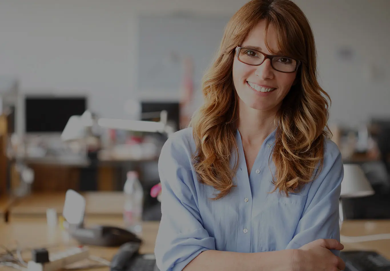A woman with long brown hair and glasses is smiling and looking at the camera